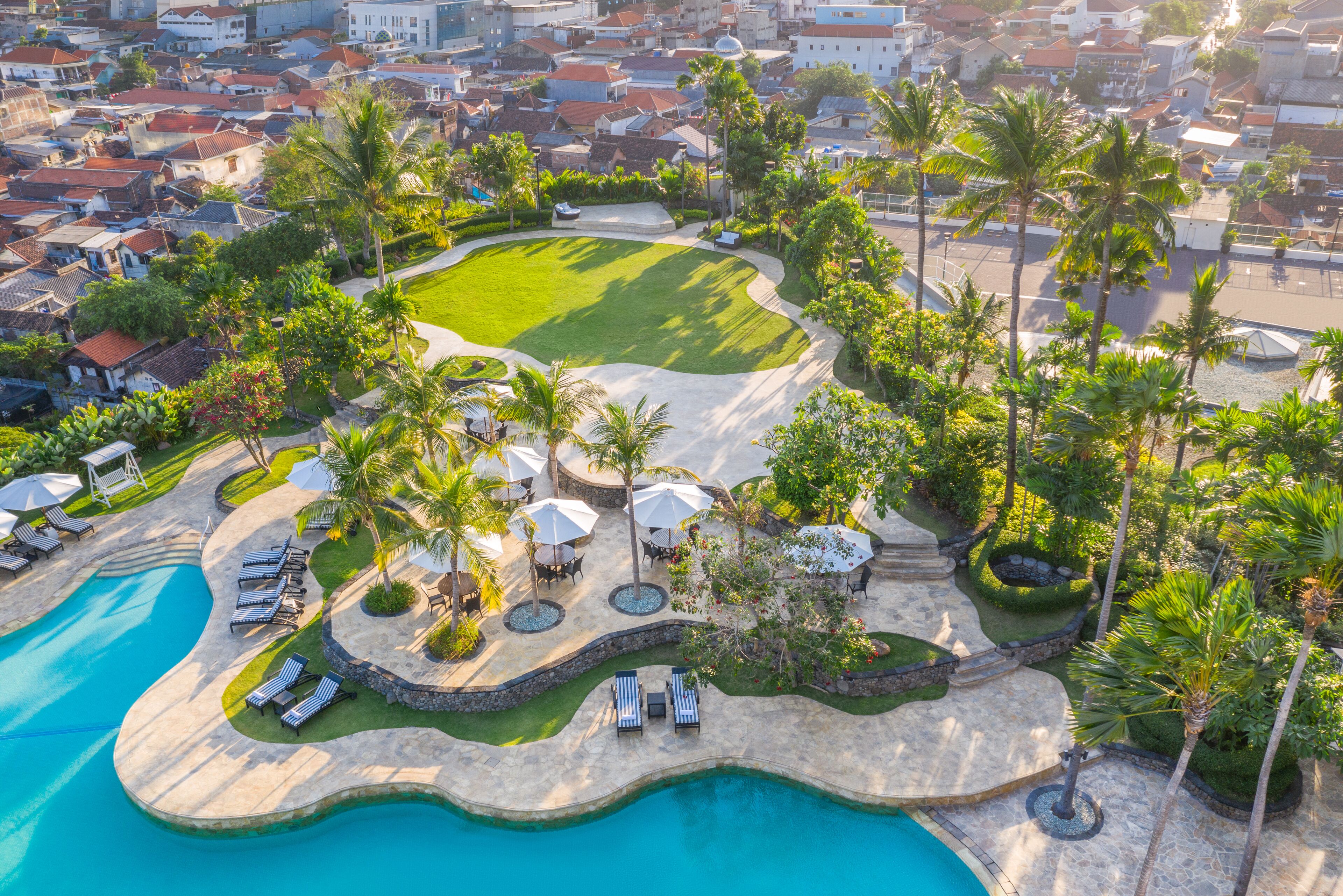 Vue aérienne d’un complexe hôtelier doté d’une piscine, de chaises longues, de palmiers et d’une pelouse bien entretenue.