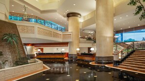 A spacious lobby with a reception desk, large columns, a palm tree sculpture, and a staircase leading to an upper level. - JW Marriott Surabaya (Surabaya)