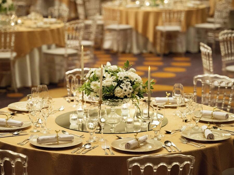 A banquet hall with round tables set for a formal event, featuring gold tablecloths, white napkins, and floral centerpieces.