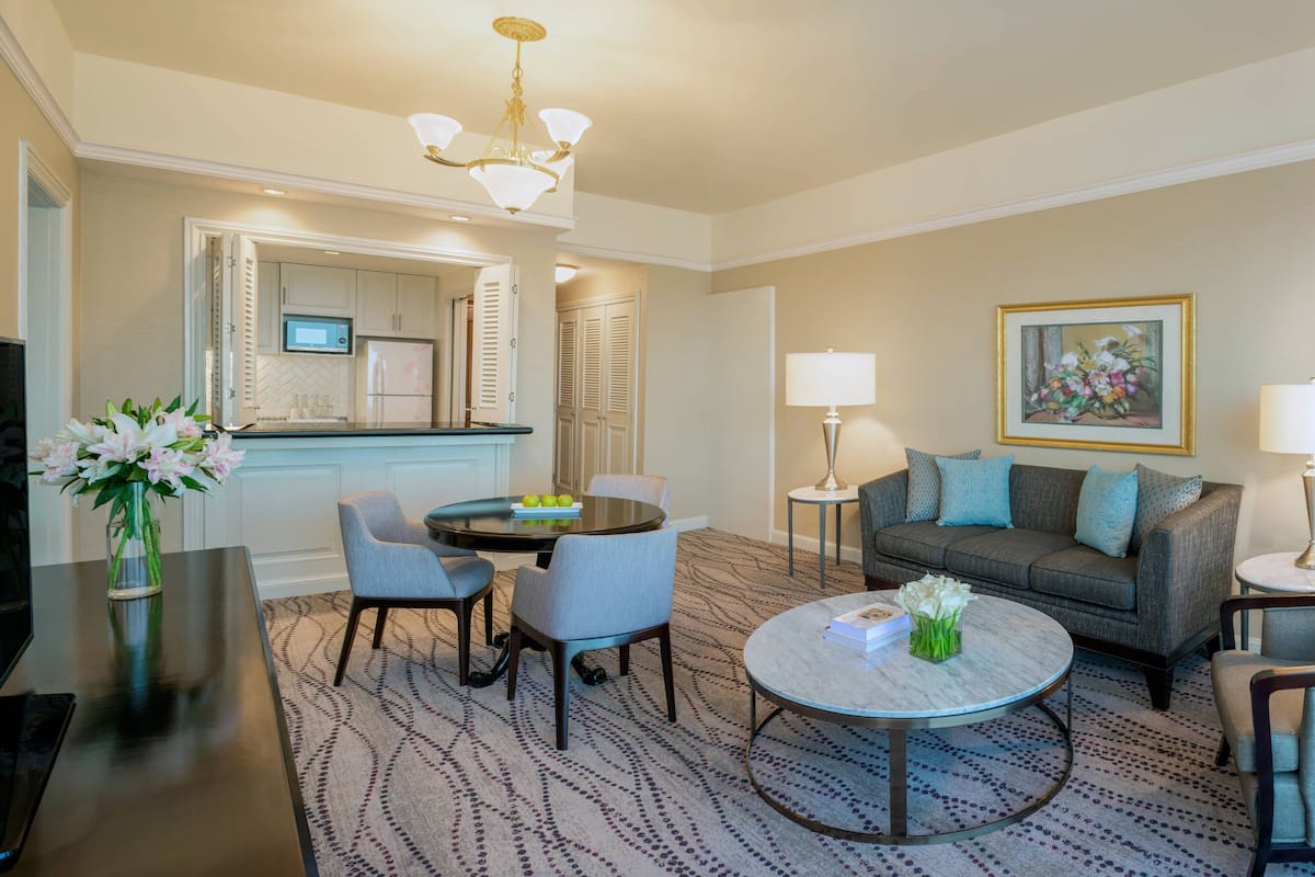 A modern hotel room with a dining area, a sofa, a coffee table, and a TV.