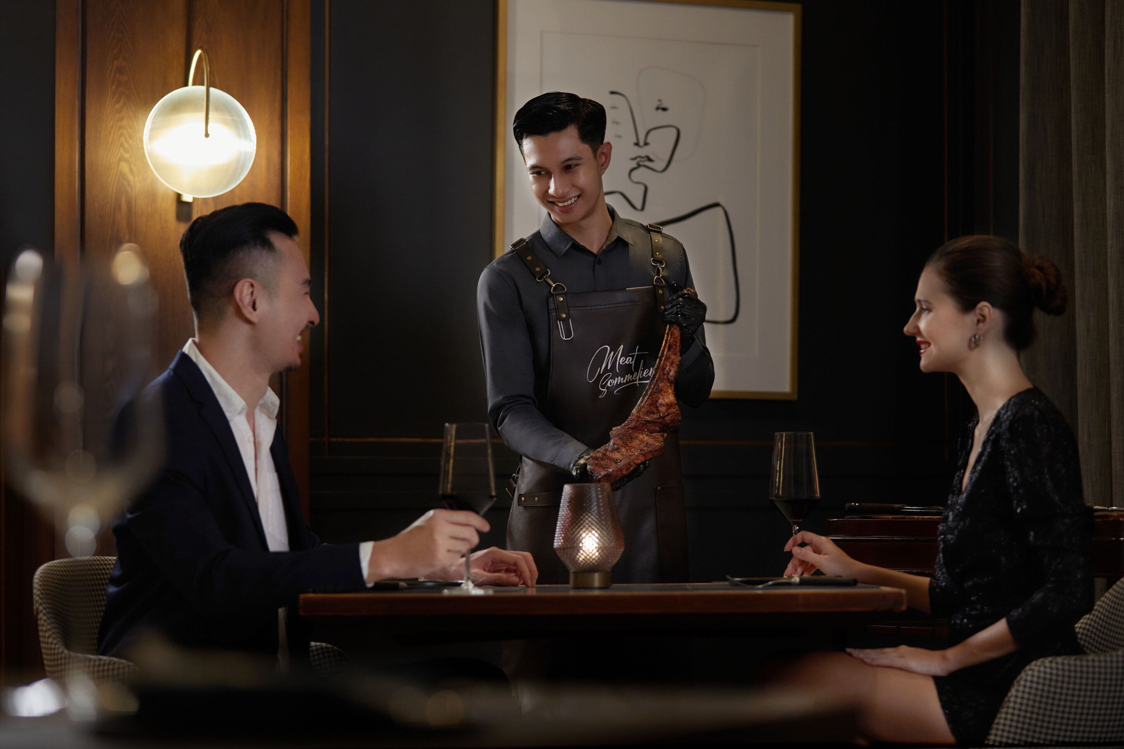 A restaurant setting with a waiter serving a dish to a seated couple.