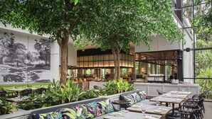 An indoor restaurant with seating arrangements, a mural, and a view of the kitchen. - JW Marriott Surabaya (Surabaya)
