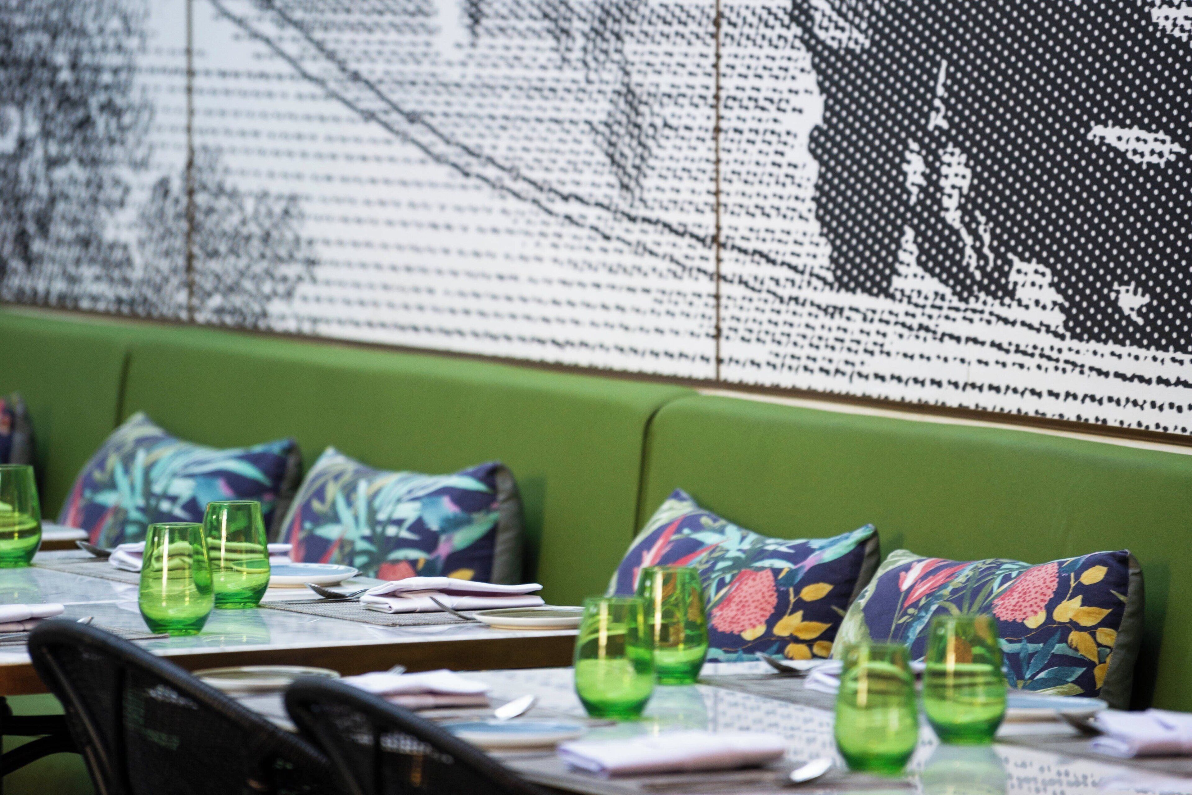 Interior de restaurant amb una llaueta amb seients acolxidats verds, vidrieres verdes i coixins estampats.