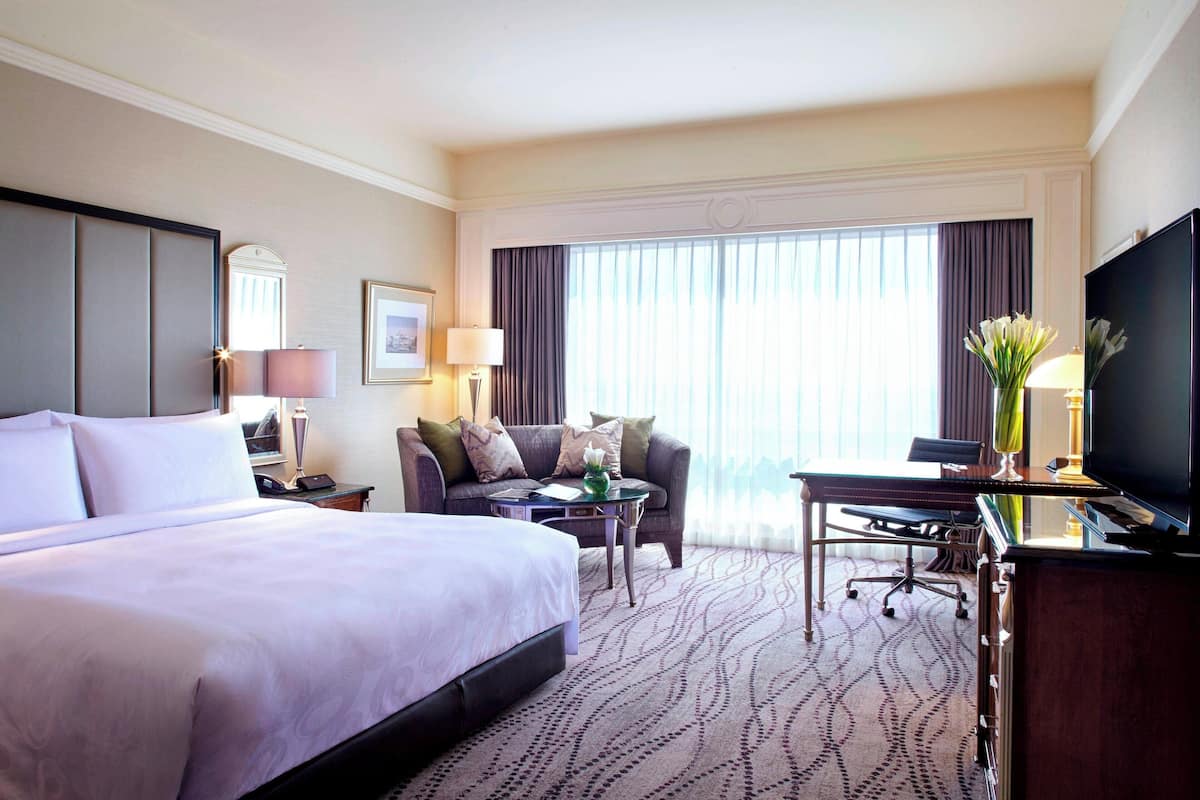 A hotel room with a large bed, a desk with a chair, a television, and a window with curtains.