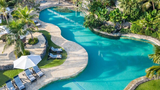 A large, winding pool with clear blue water, surrounded by palm trees and lounge chairs. - JW Marriott Surabaya (Surabaya)