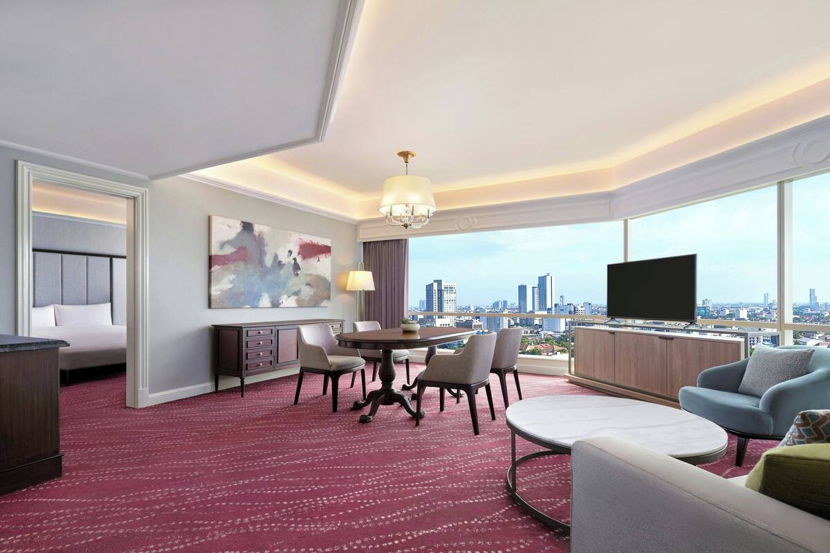 A hotel room with a city view, a dining area, a TV, and a large window.