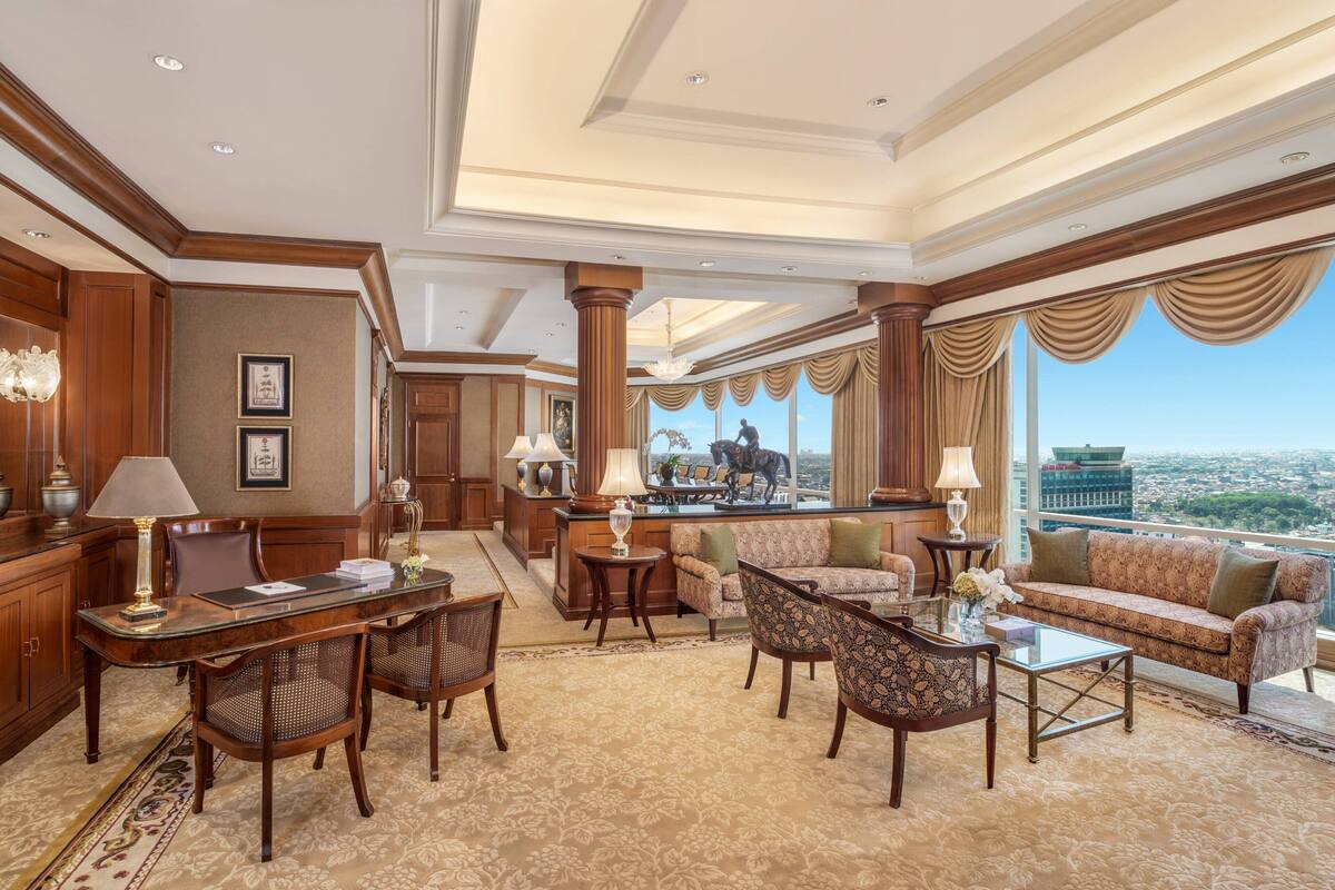 A spacious living area with a large window offering a city view, a dining area with a table and chairs, and a seating area with sofas and a coffee table.