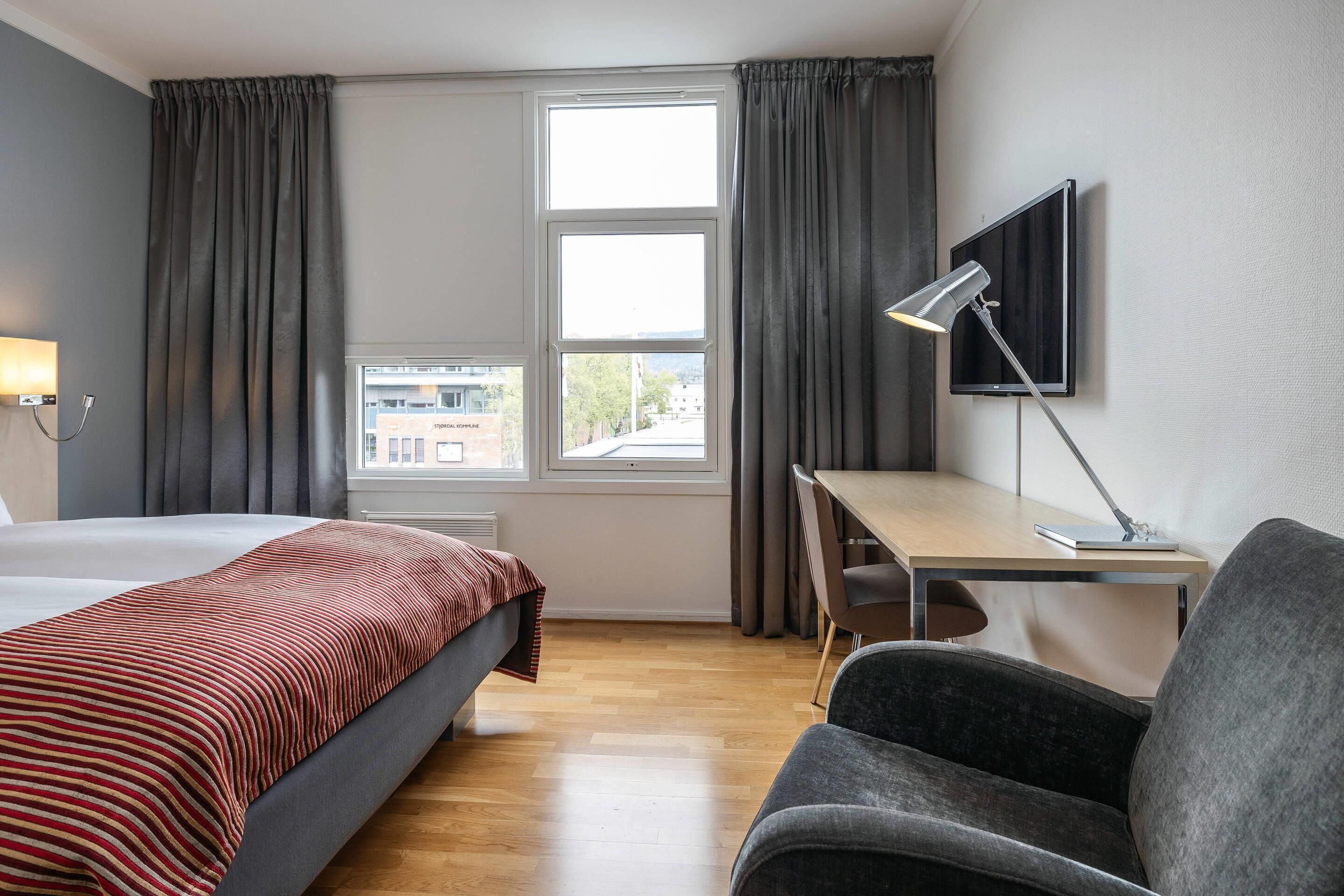 Een hotelkamer met een bed, een bureau, een stoel, een televisie en een raam met gordijnen.
