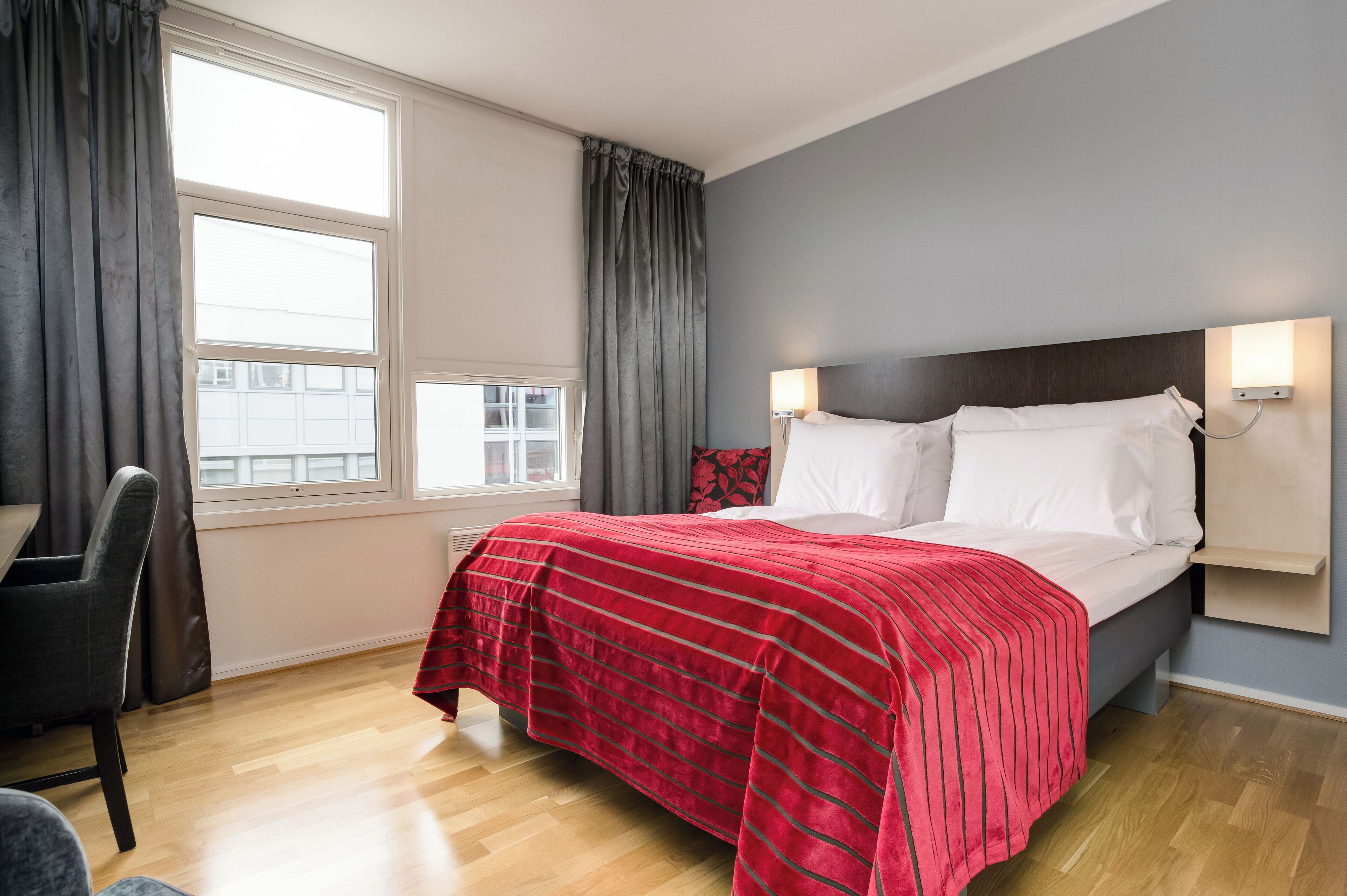A hotel room with a bed, a desk, and a window with curtains.