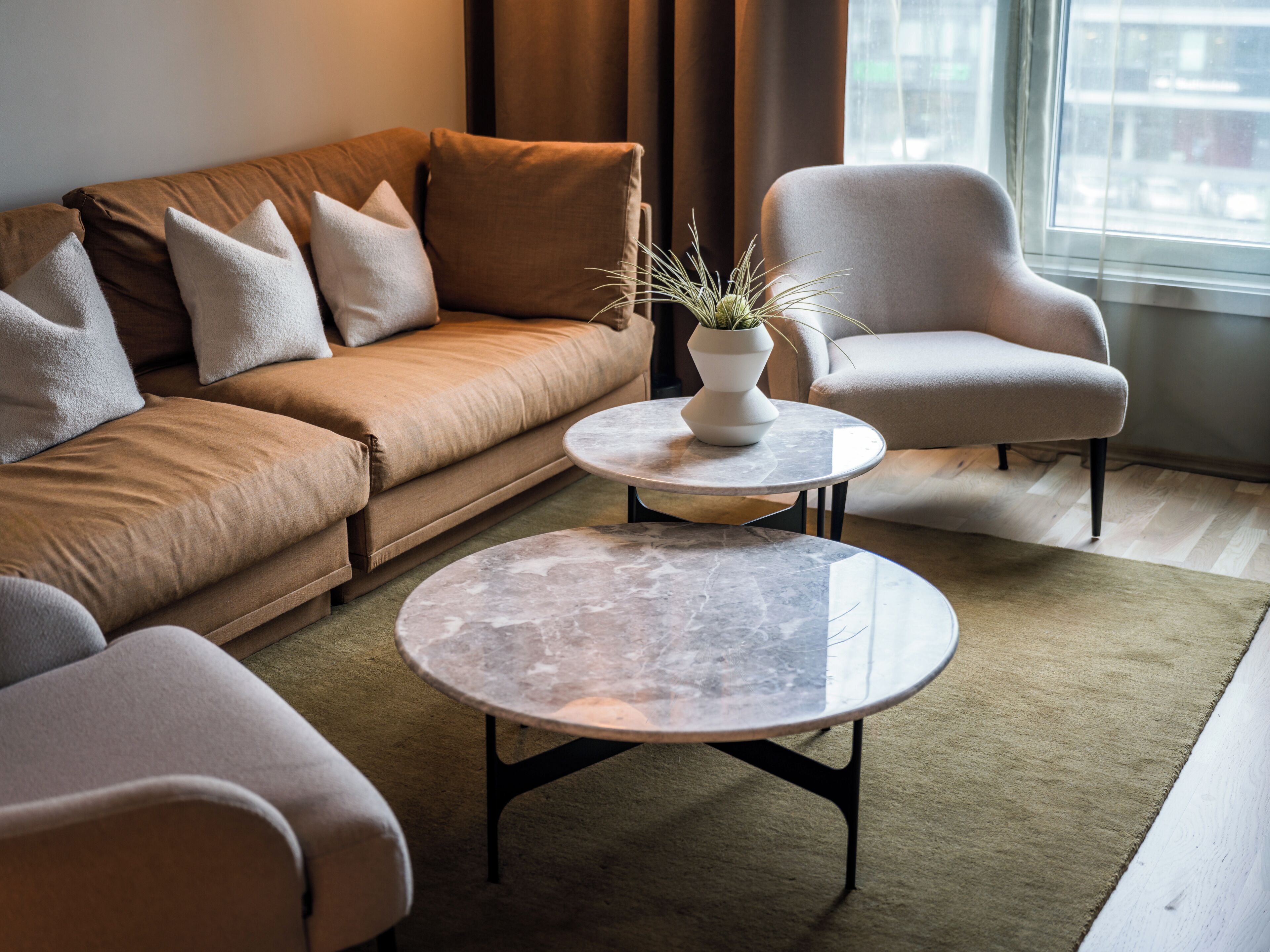 A modern living room with a sofa, armchair, round coffee table, and a potted plant.