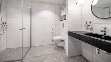 Un baño moderno con ducha acristalada, inodoro y lavamanos sobre encimera negra.
