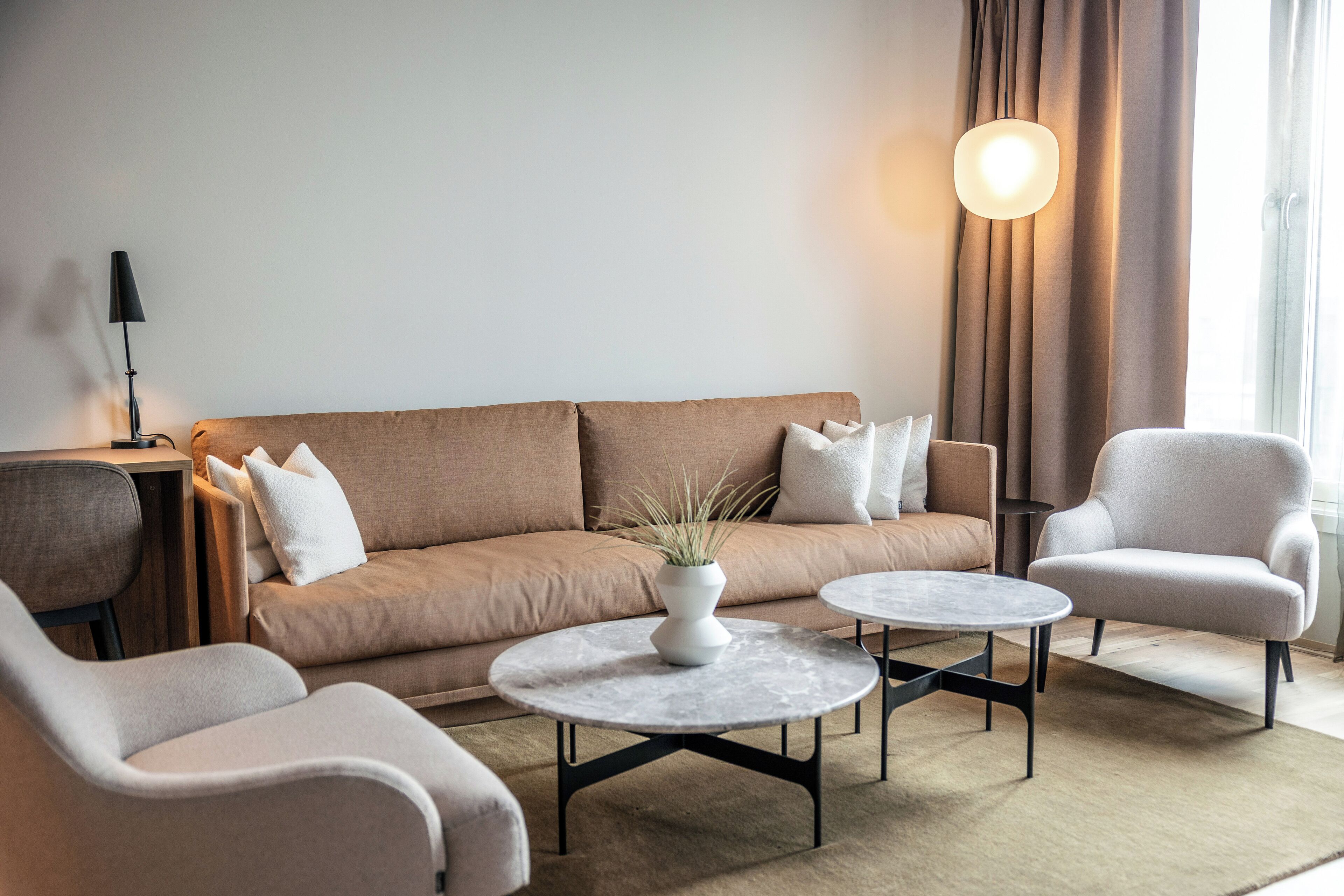 A modern living room with a beige sofa, two armchairs, a coffee table, and a floor lamp.