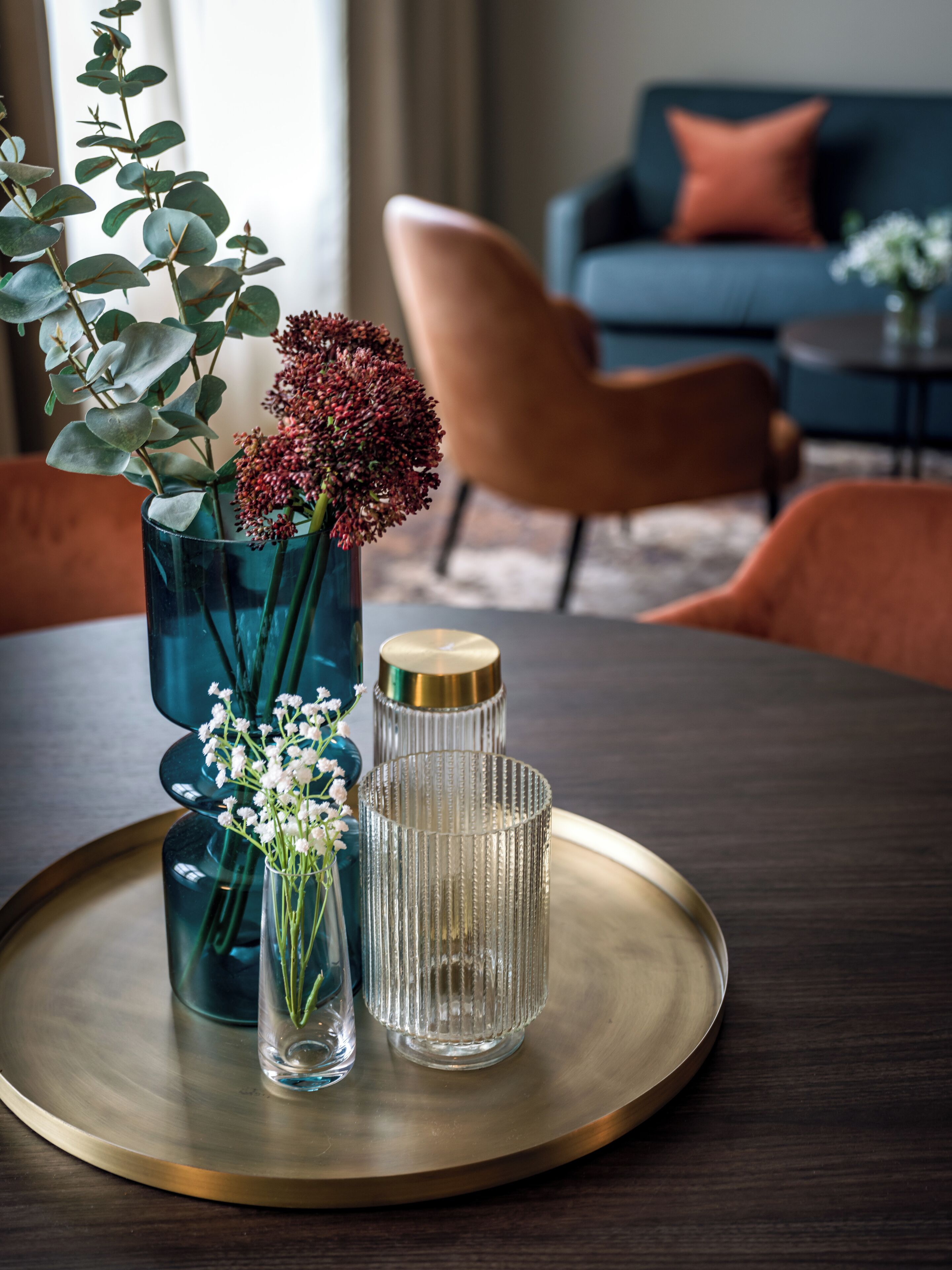 Een eettafel met een dienblad, een blauwe vaas met bloemen en een glazen vaas.