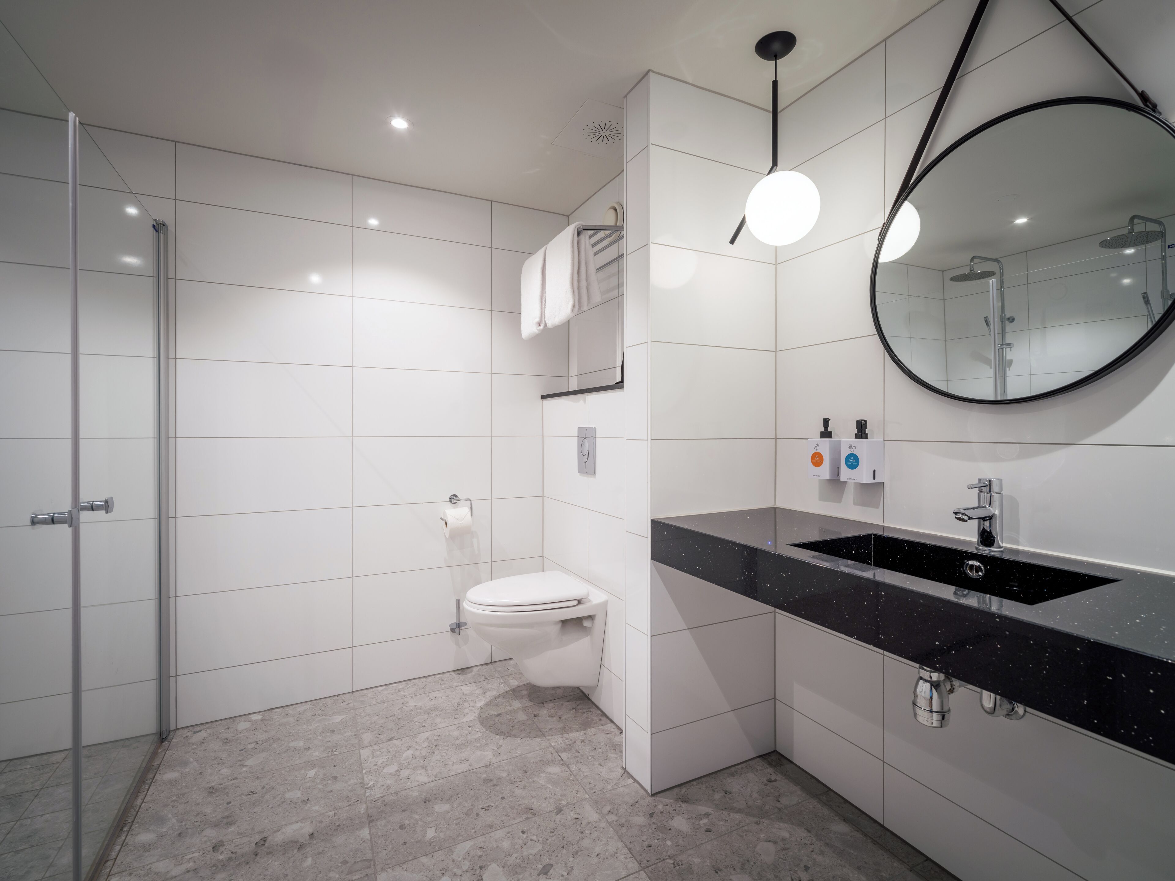 Ein modernes Badezimmer mit Toilette in Weiß, einem schwarzen Waschtisch und einer Duschkabine.