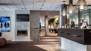 Un vestíbulo moderno con chimenea, una recepción y un cuadro grande de personas caminando.