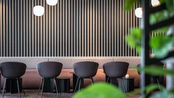 A modern interior with a row of dark chairs, a cushioned bench, and a vertical striped wall with hanging lights.
