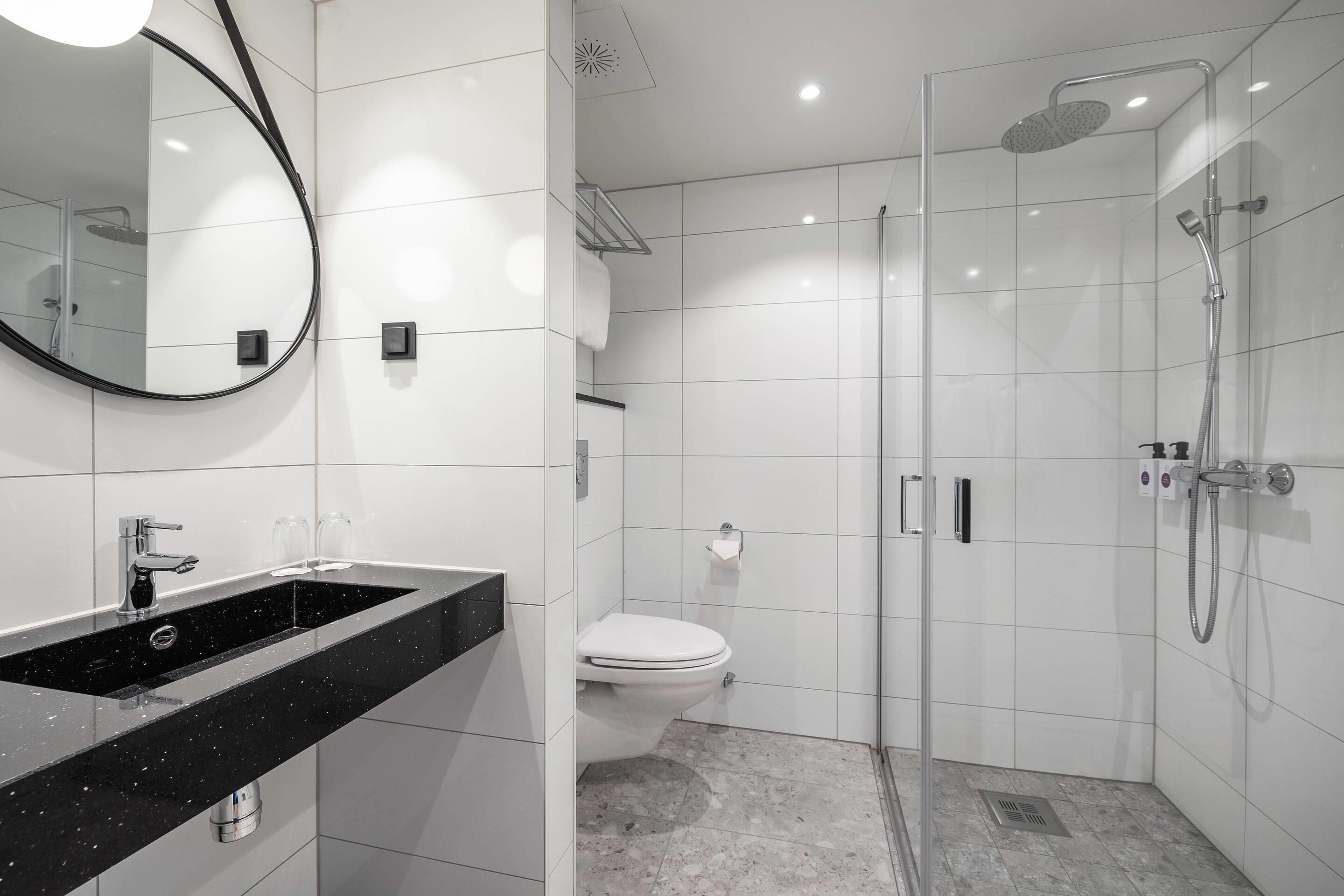 Un baño moderno con lavamanos de encimera negro, inodoro, ducha con cerramiento de vidrio y un espejo grande.