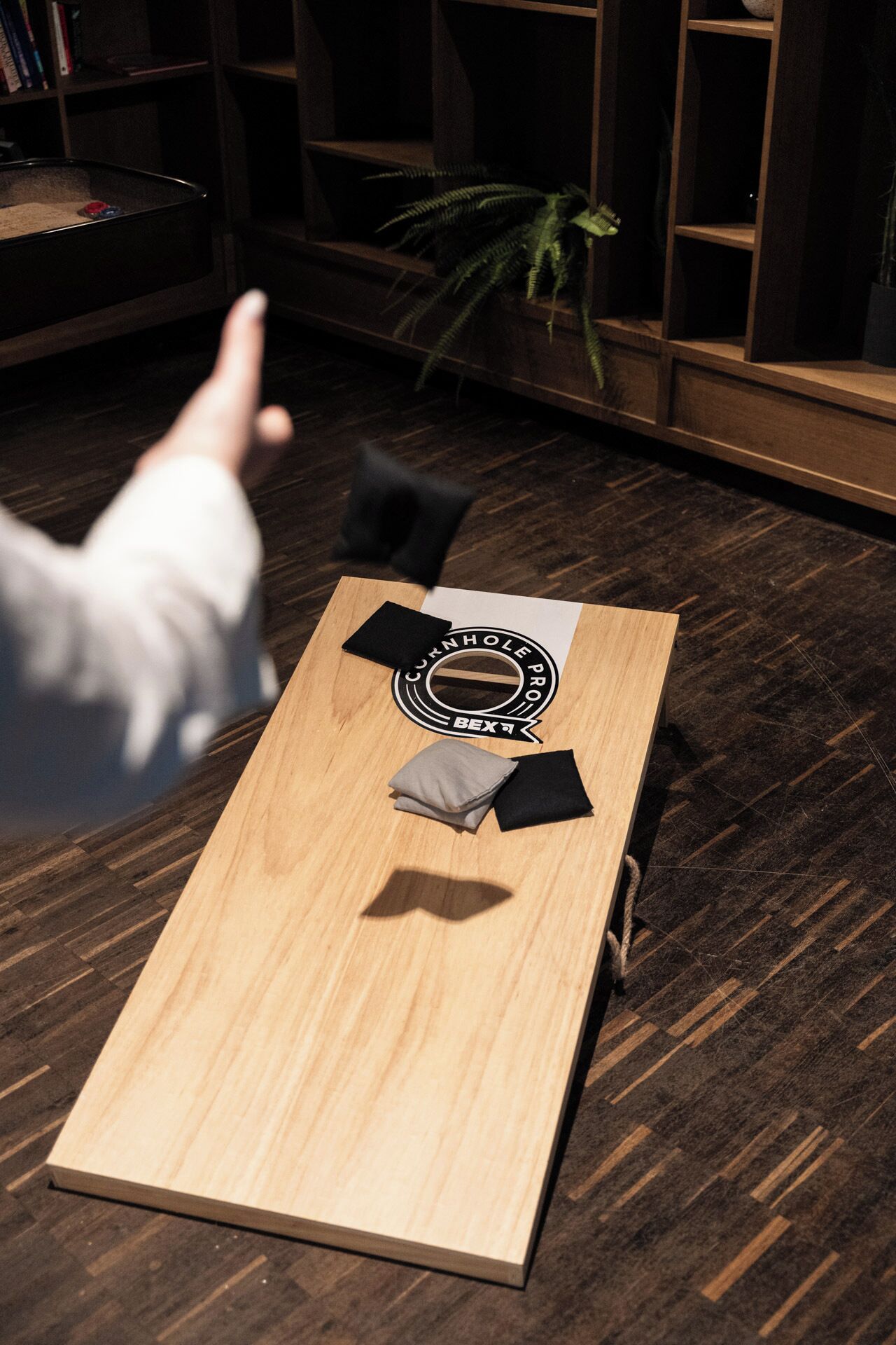 A wooden table with a logo, a black chair, and a potted plant in a room with dark wooden flooring and bookshelves.