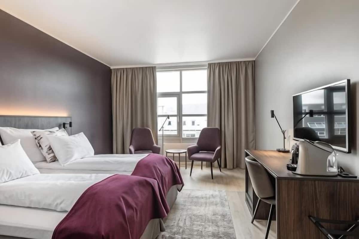 Una habitación de hotel con dos camas, un escritorio, una silla, un televisor y un ventanal con cortinas.