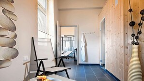 A modern spa room with a stone wall, a white table with candles, a black chair, and a wooden wall with a decorative vase. - Wyndham Duisburger Hof (Duisburg)