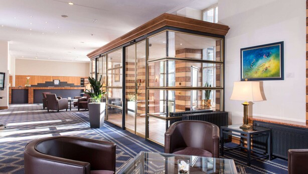 A hotel lobby with a reception desk, seating area, and a large glass partition. - Wyndham Duisburger Hof (Duisburg)
