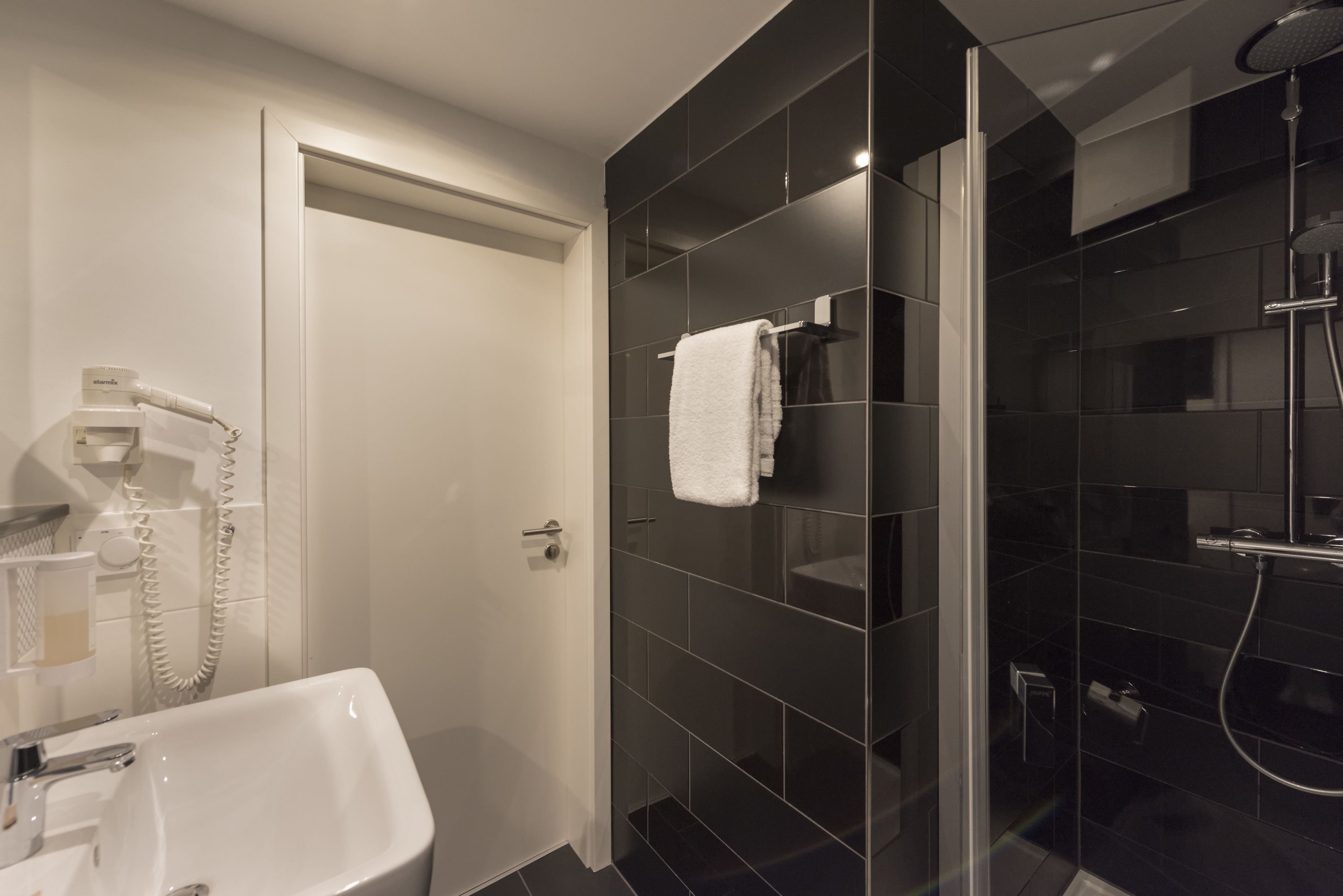 Un baño moderno con un lavamanos blanco, cabina de ducha con mampara de cristal y una toalla colgada en la pared.