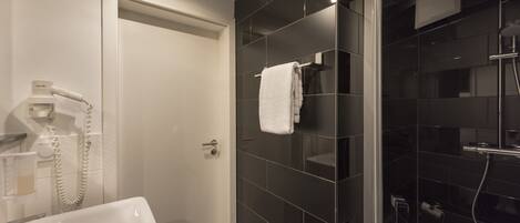 Un baño moderno con un lavamanos blanco, cabina de ducha con mampara de cristal y una toalla colgada en la pared.