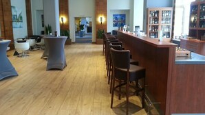 A modern bar area with wooden flooring, bar stools, and a counter with a minibar. - Wyndham Duisburger Hof (Duisburg)