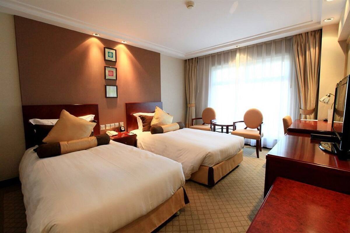 A hotel room with two beds, a desk, a chair, and a television.