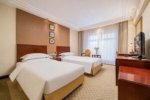 Habitación de hotel con dos camas, un escritorio, una silla, un televisor y una ventana con cortinas.
