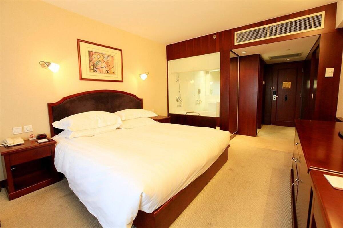 Habitación de hotel con una cama grande, una mesita de noche con teléfono, un espejo y una puerta que da al baño.