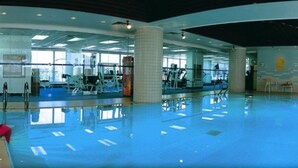 A large indoor swimming pool with clear blue water, surrounded by exercise equipment and a high ceiling with skylights. - Beijing Landmark Hotel (Beijing)