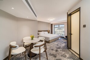 Une chambre d’hôtel avec un lit, une petite table ronde avec des chaises, un vase de fleurs et une vue sur la ville par la fenêtre.
