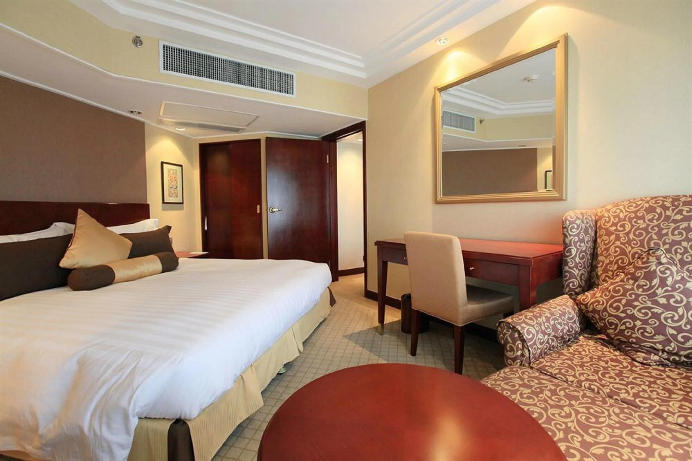 Habitación de hotel con cama, escritorio, silla y un espejo grande.