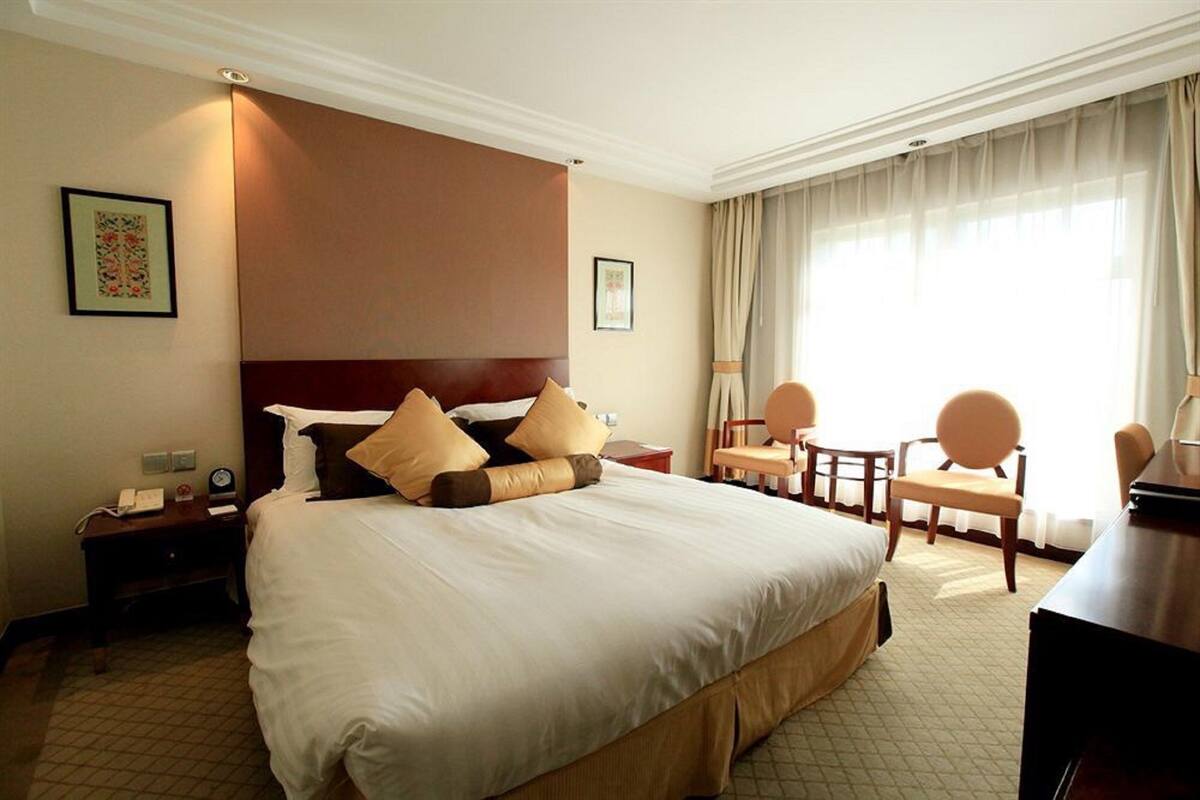 Habitación de hotel con una cama grande, dos sillas, un escritorio y una ventana con cortinas.