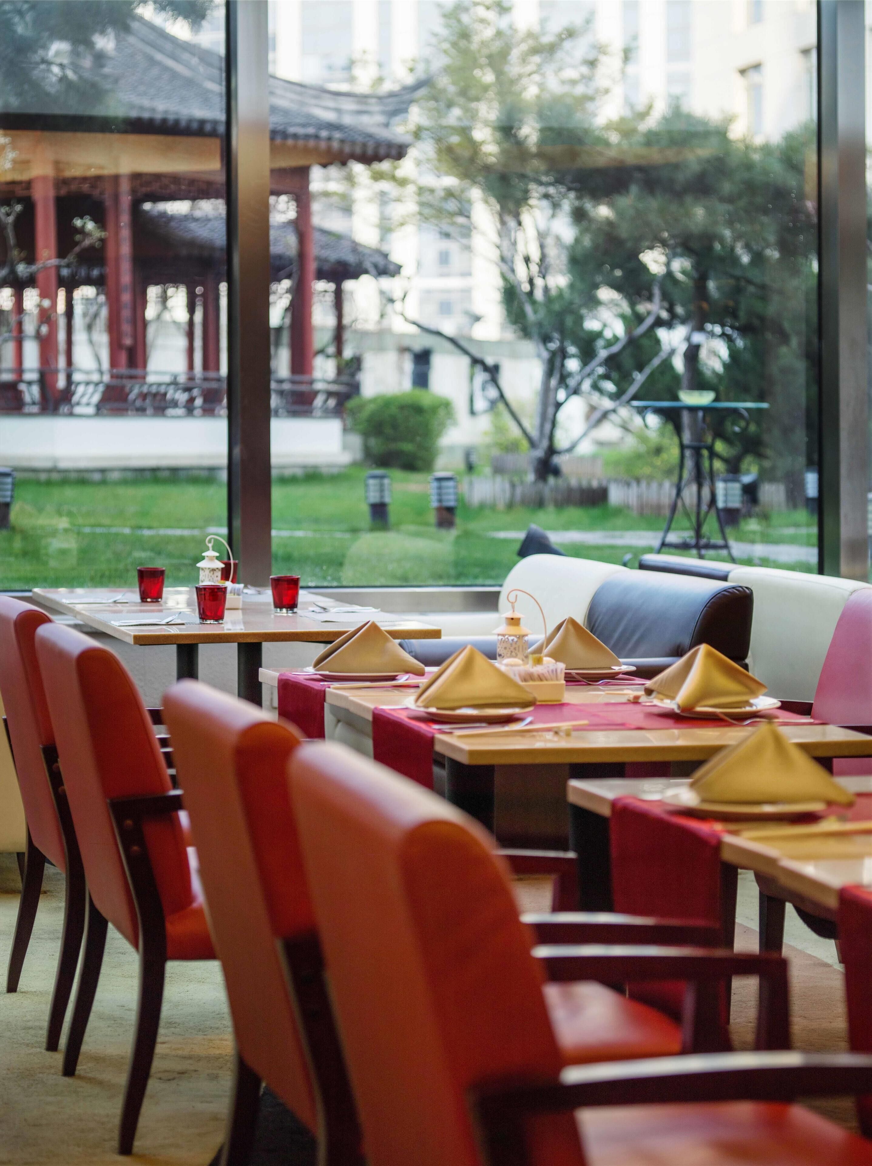 Un restaurant avec des tables dressées, des chaises et une vue sur un bâtiment traditionnel et la verdure environnante.