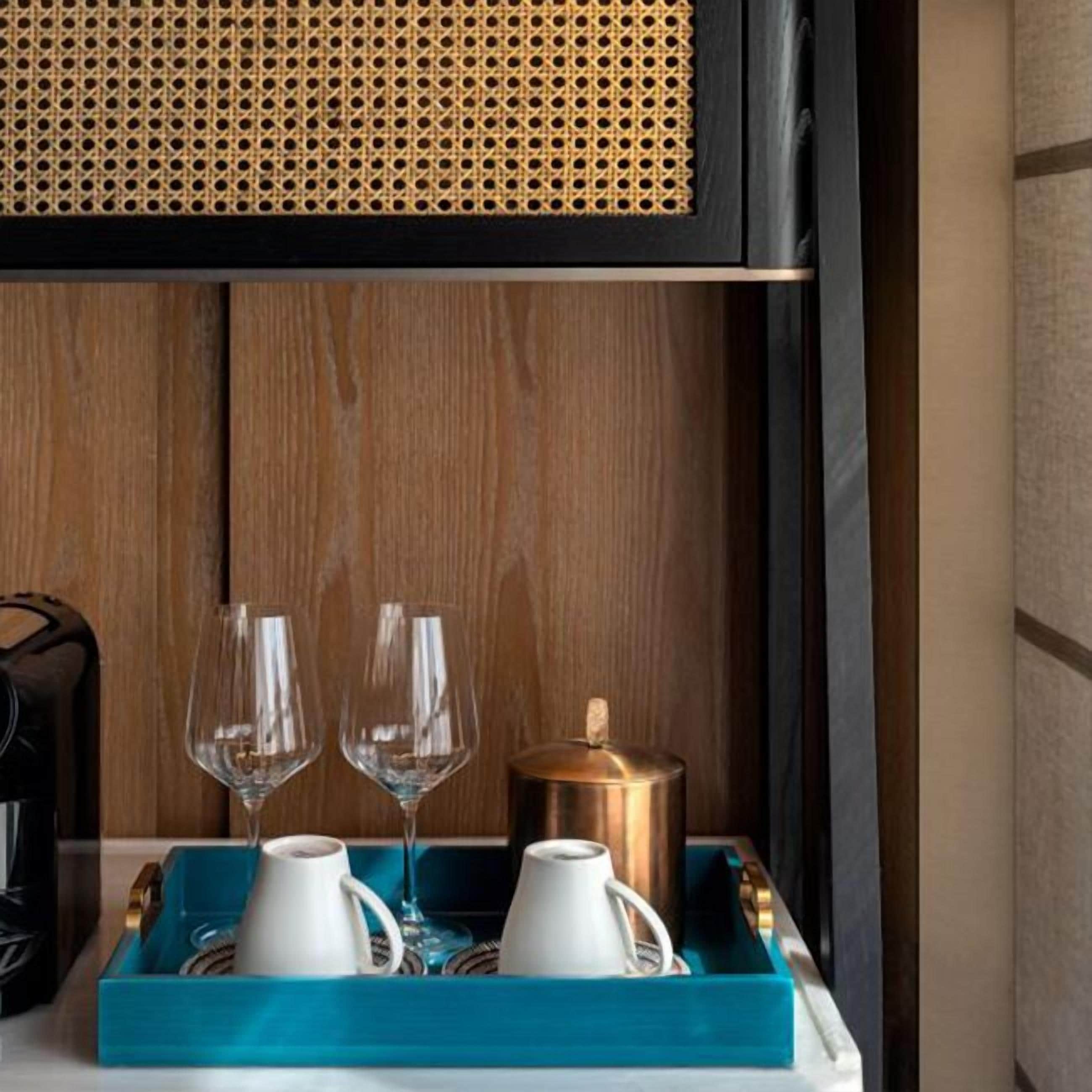 Una bandeja azul con dos tazas blancas y un recipiente dorado, sobre un panel de madera.