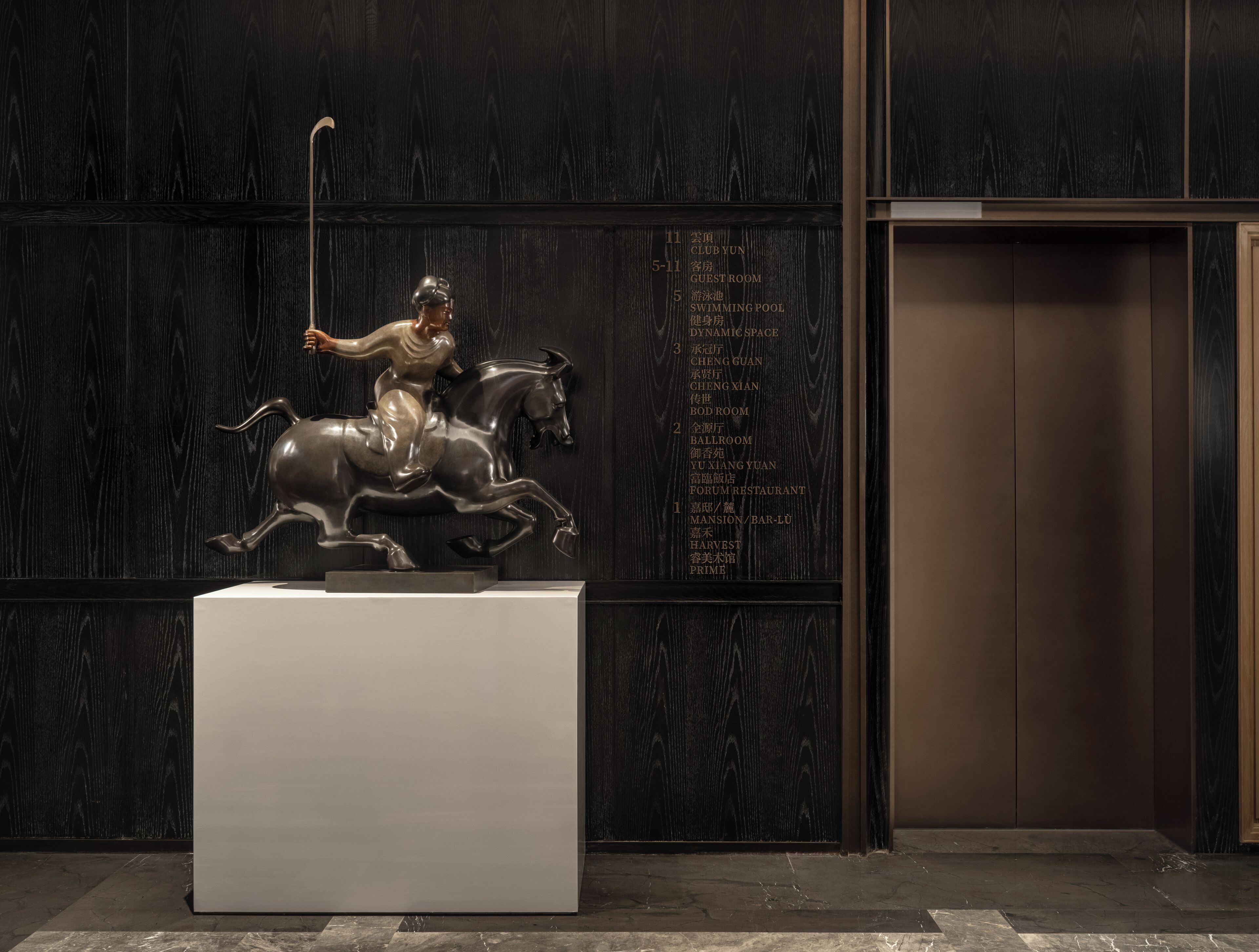 A sculpture of a figure on horseback in a lobby with a marble floor and a wooden wall with a list of room names.
