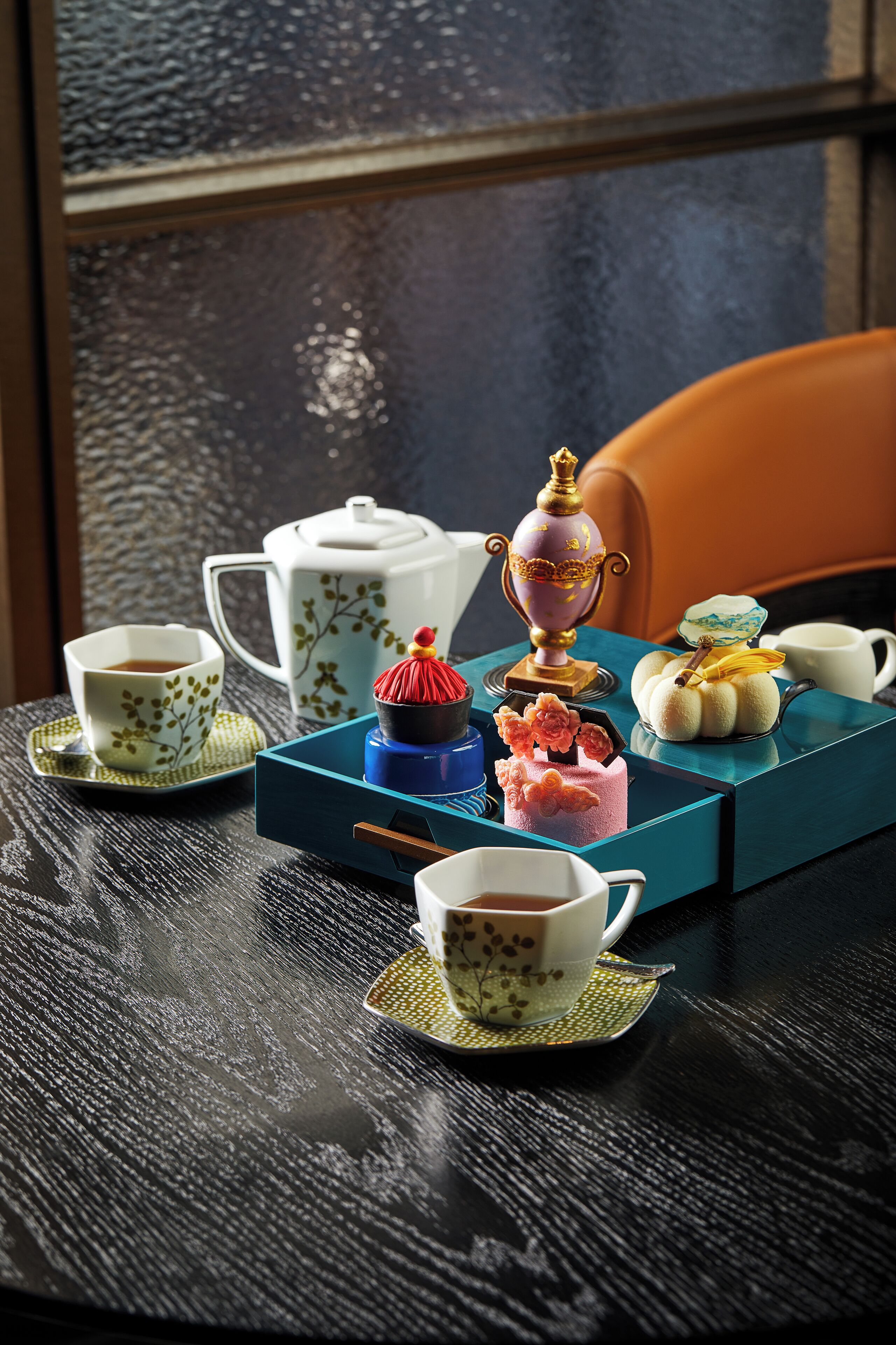 A table with a teapot, cups, a decorative box, and a chair.