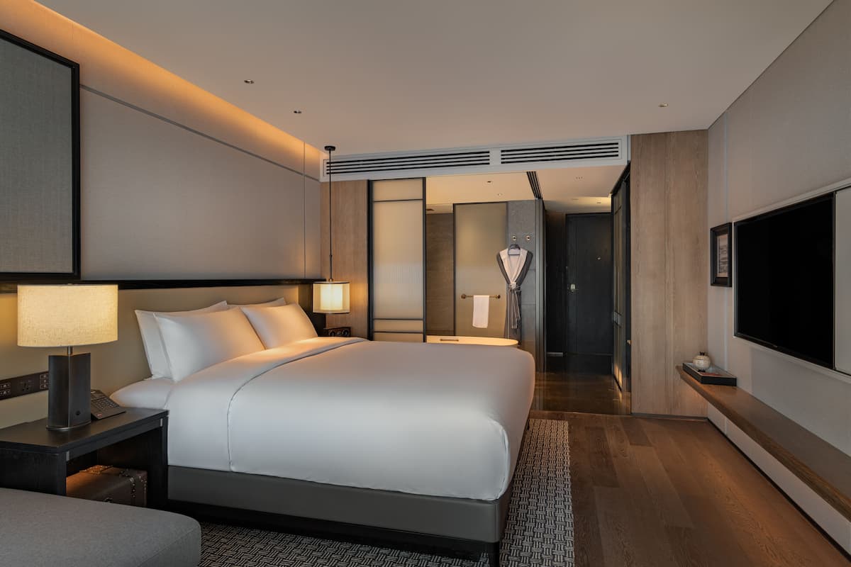 A modern hotel room with a large bed, bedside tables, a TV, and a bathroom with a shower and toilet.