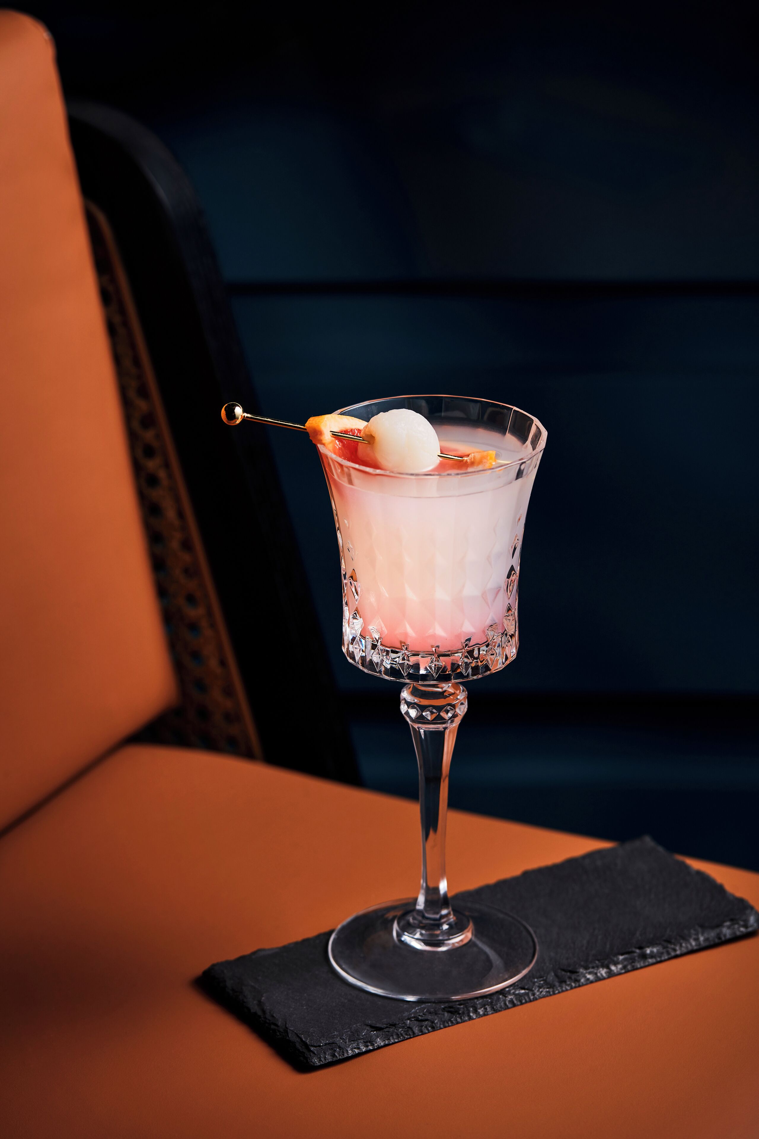 A cocktail in a glass with a decorative stick, placed on a black napkin on a chair.