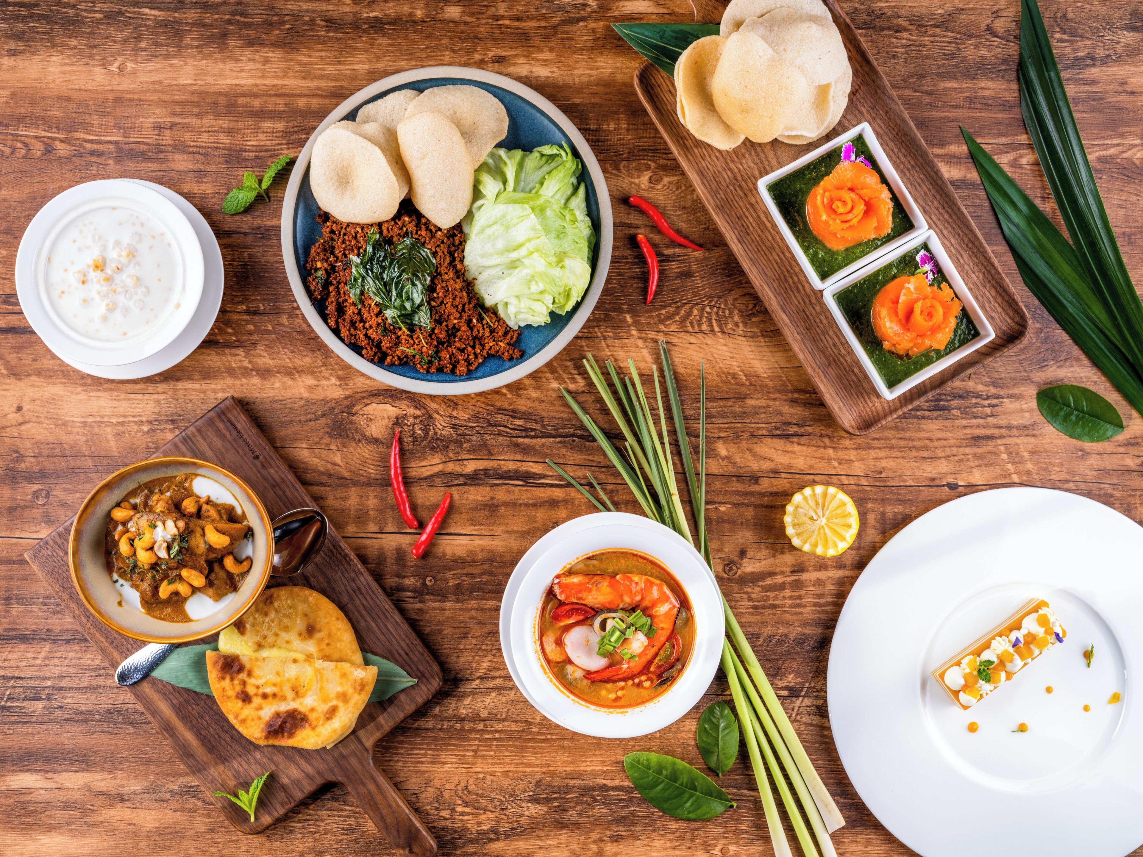 Una mesa de madera con diversos platos, incluyendo un tazón de curry, una fuente de pan plano y un tazón de sopa.