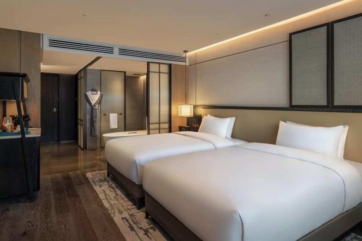 A hotel room with two beds, a desk, and a mirror.