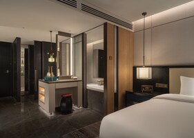 A modern hotel room with a large bed, a vanity with a mirror, a sink, and a small table with a radio.