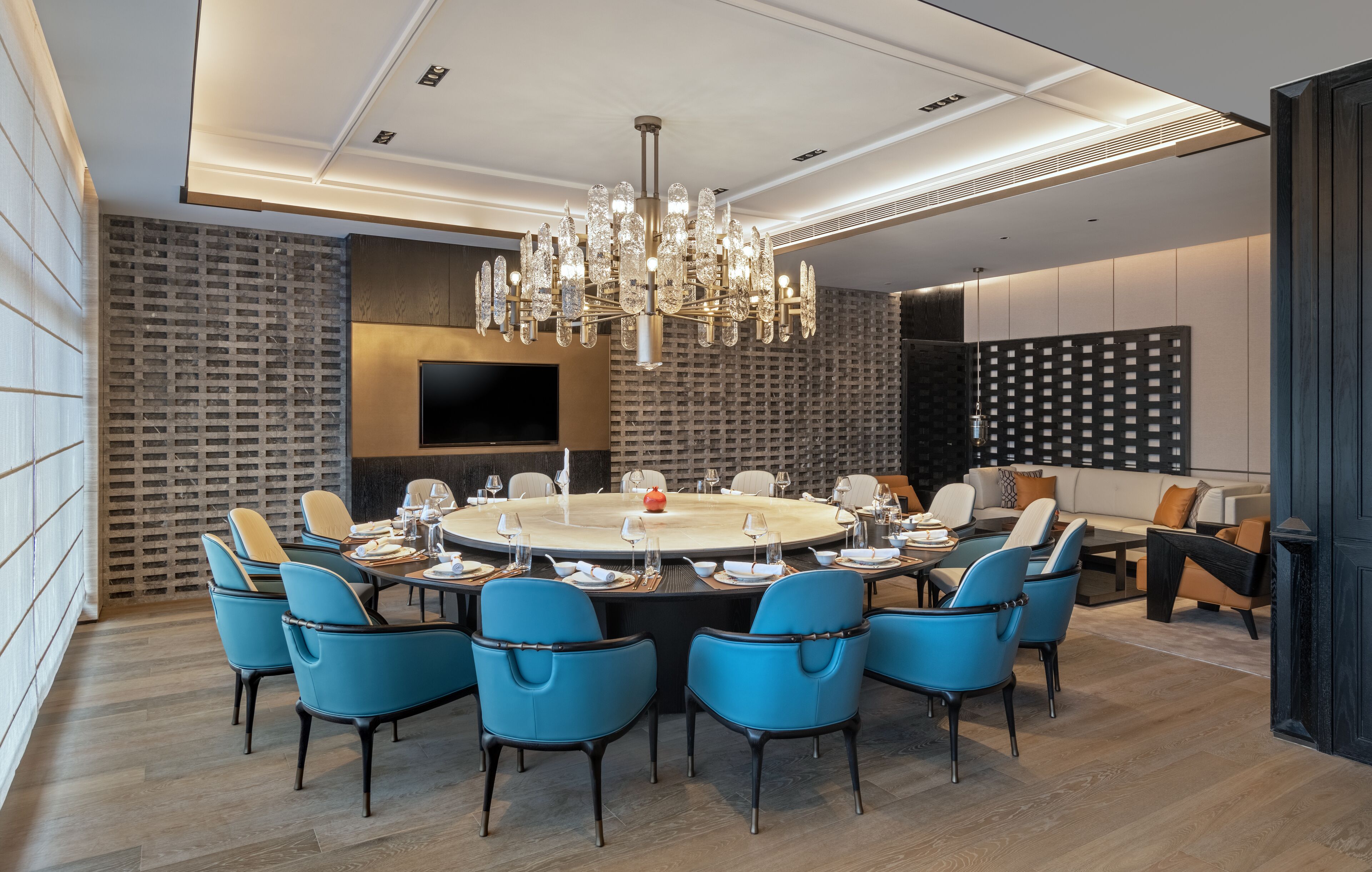 A modern dining area with a round table, blue chairs, and a chandelier.