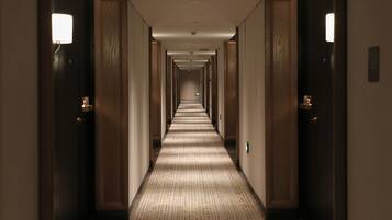 Um corredor de hotel comprido e estreito, com portas de madeira e luminárias em ambos os lados.