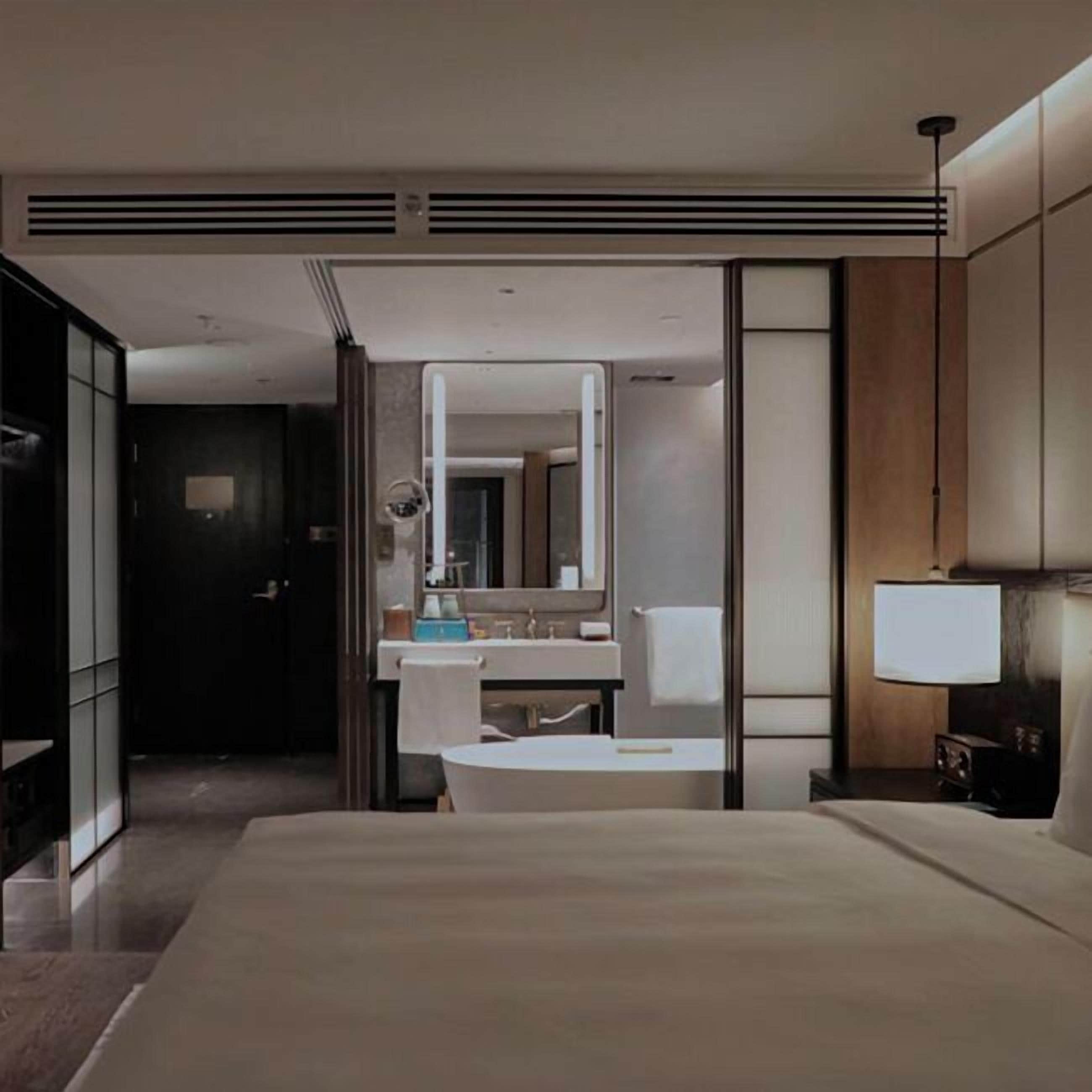 Una camera d'albergo moderna con un letto grande, un bagno con uno specchio e un comodino.