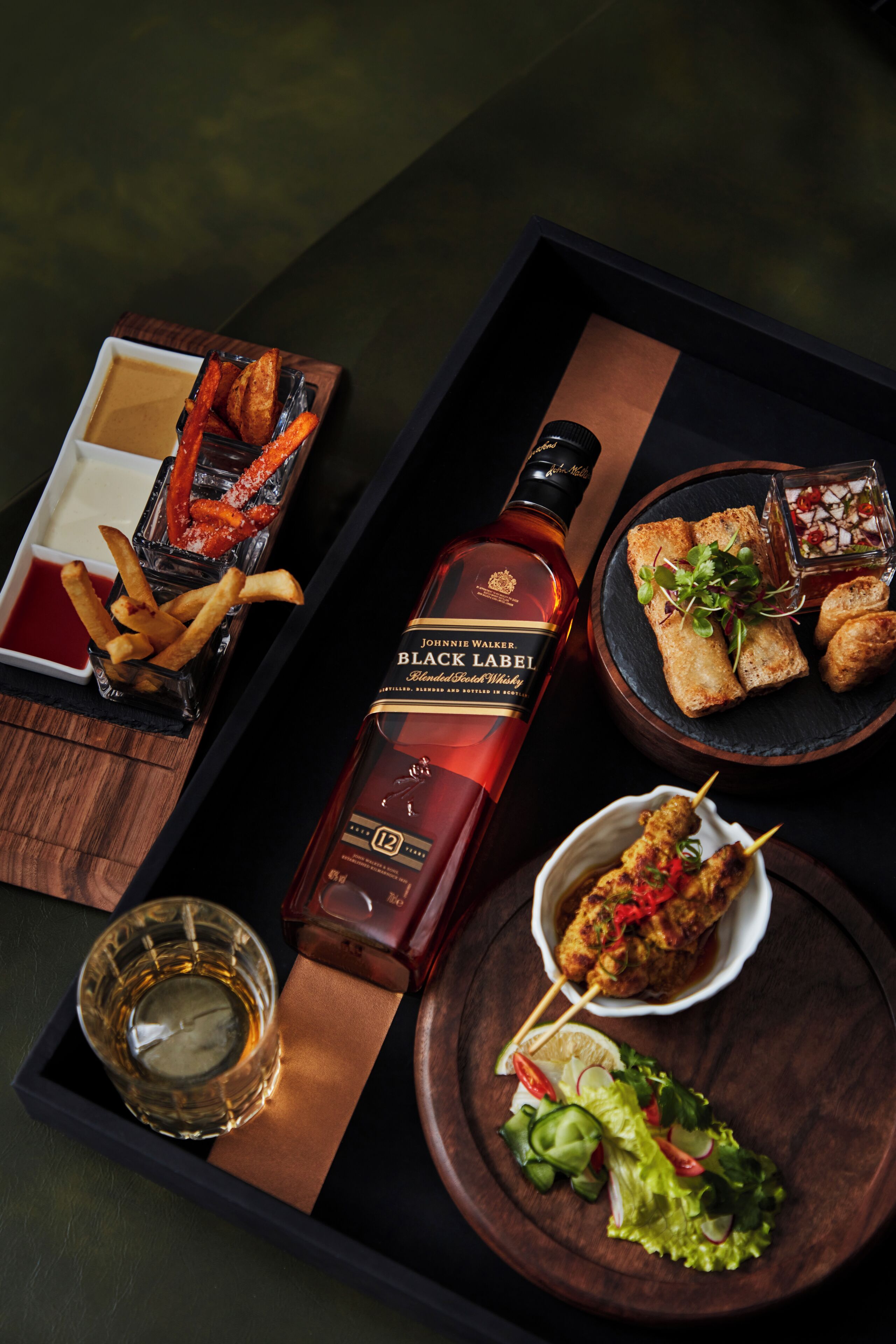 Uma bandeja com diversos alimentos e uma garrafa de whisky Johnnie Walker Black Label.