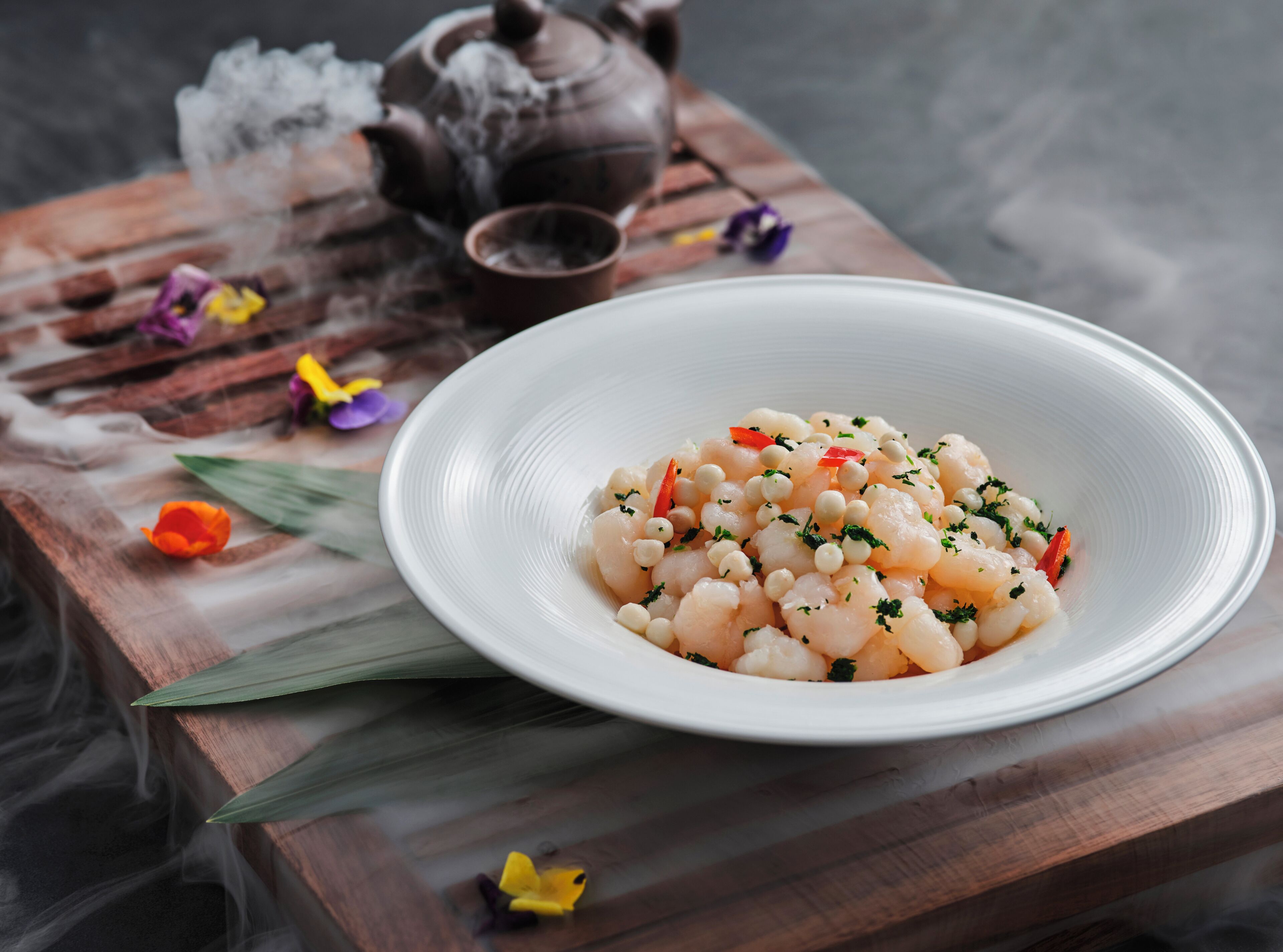 A white plate with a seafood dish, a teapot, and a cup on a wooden table.