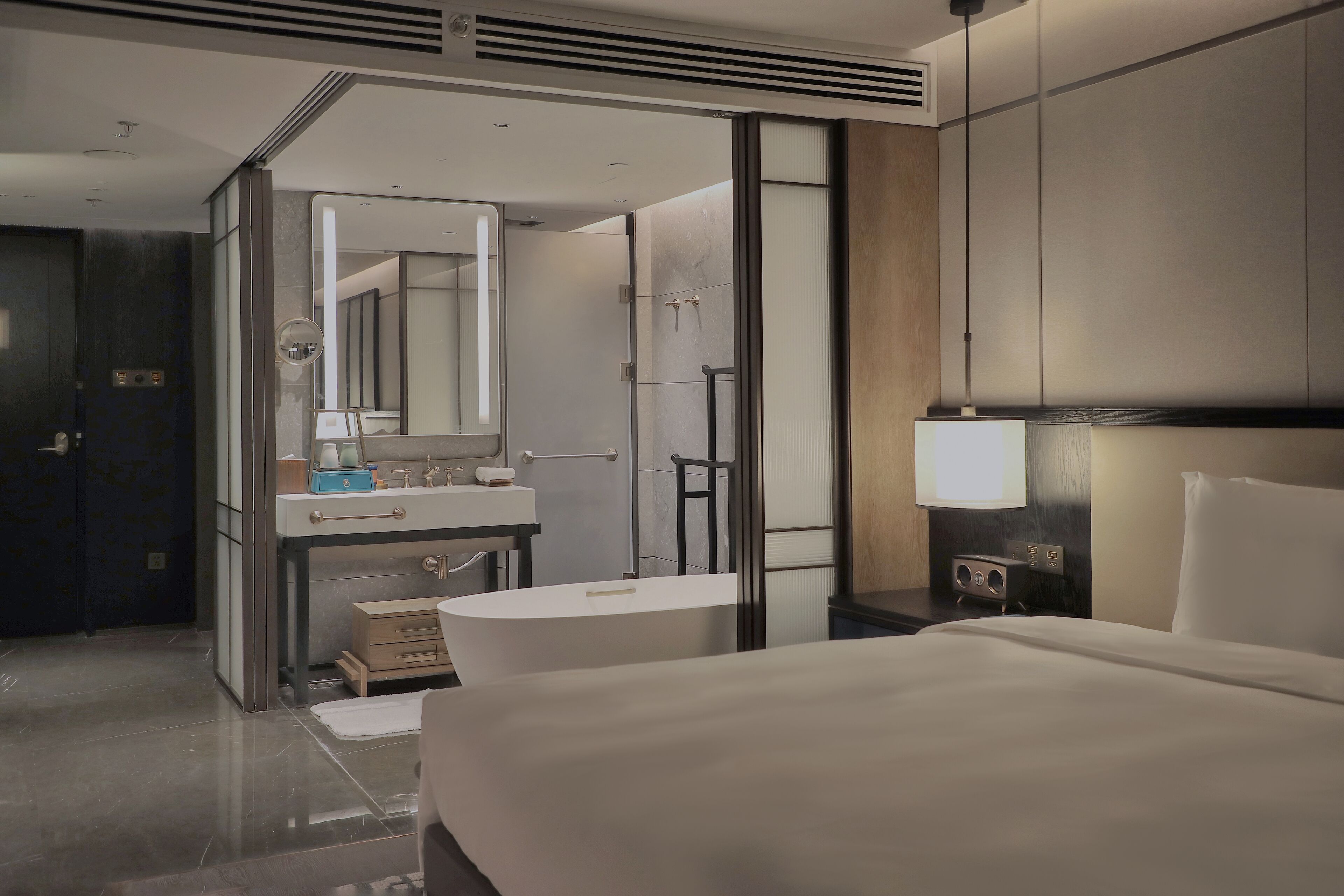 Et moderne hotelværelse med en stor seng, et badeværelse med badekar, et toiletbord med spejl og et sengebord med lampe.